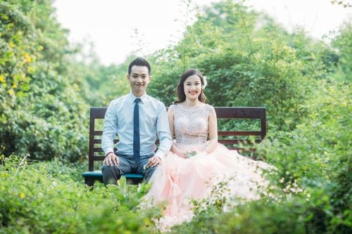 Free A couple elegantly dressed sits on a bench amidst lush greenery, radiating happiness. Stock Photo