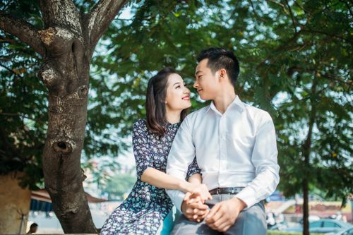 Free A happy couple sitting under a tree in a sunny park sharing a loving gaze. Stock Photo