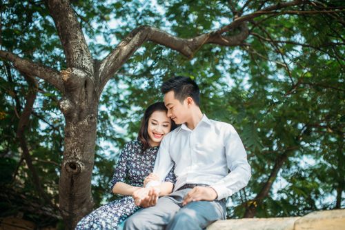 Free A young couple sharing a tender moment seated under a lush tree during daytime. Stock Photo