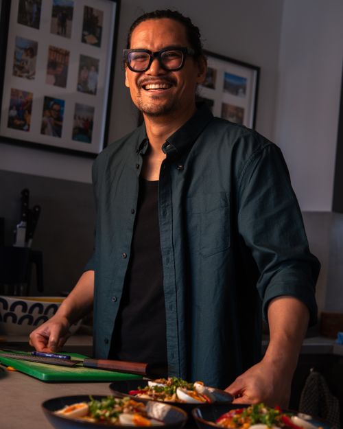 Free A cheerful chef preparing colorful Asian dishes in a cozy kitchen setting. Stock Photo