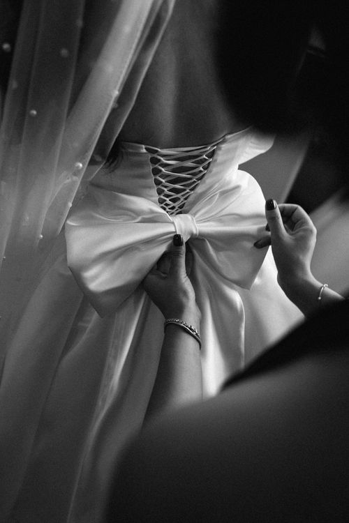 Free Black and white close-up of a bride's dress being adjusted, showing lace-up back and large satin bow. Stock Photo