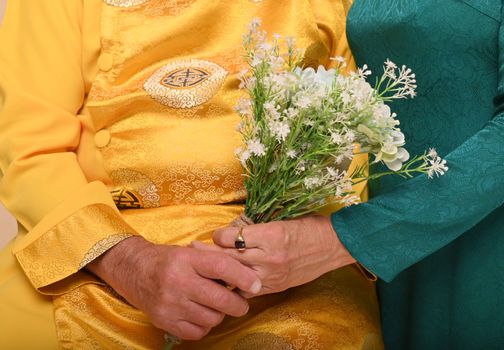 A senior couple in traditional clothing holds a bouquet, symbolizing love and togetherness.