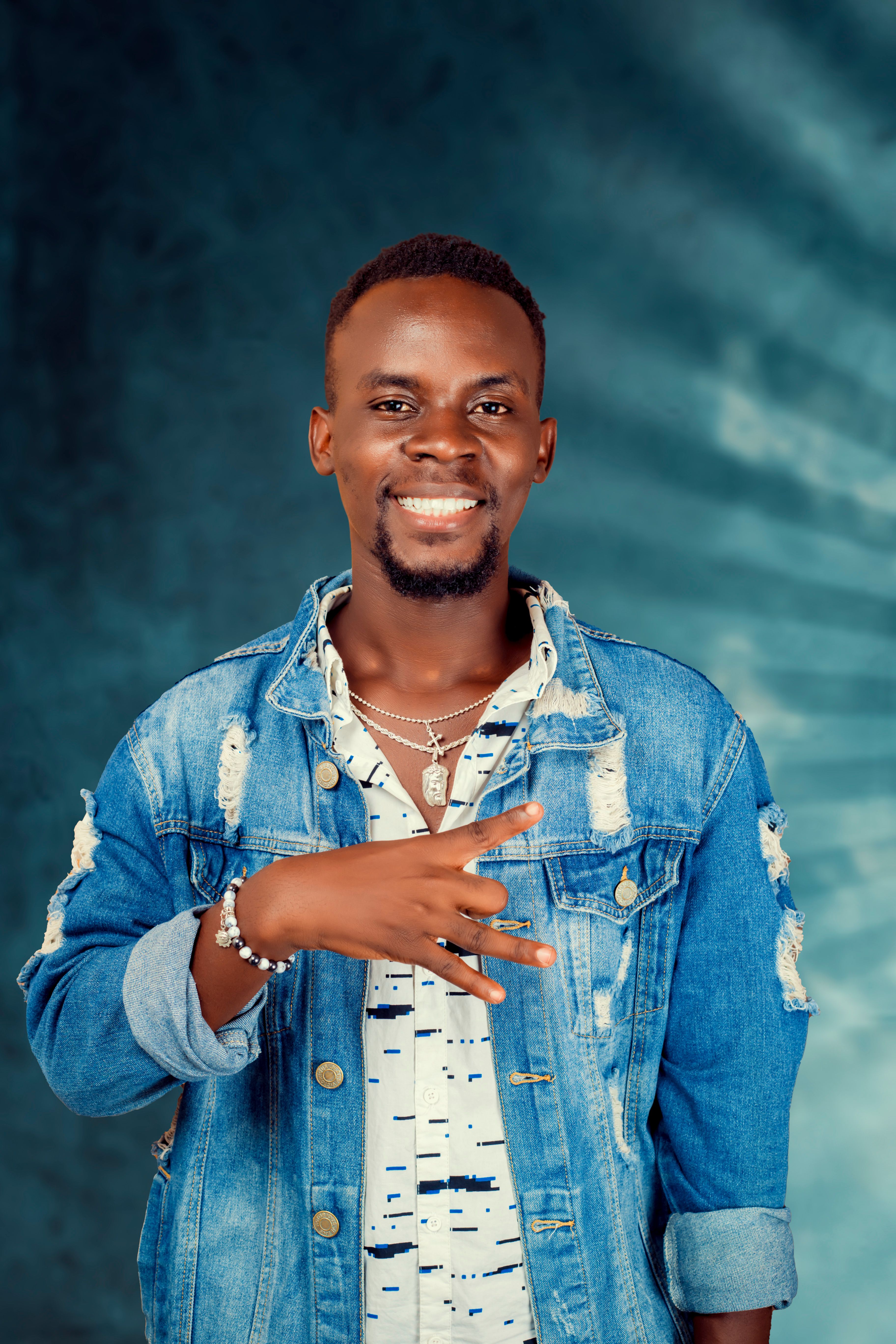 Portrait of a smiling man wearing a denim jacket with a peace sign gesture.