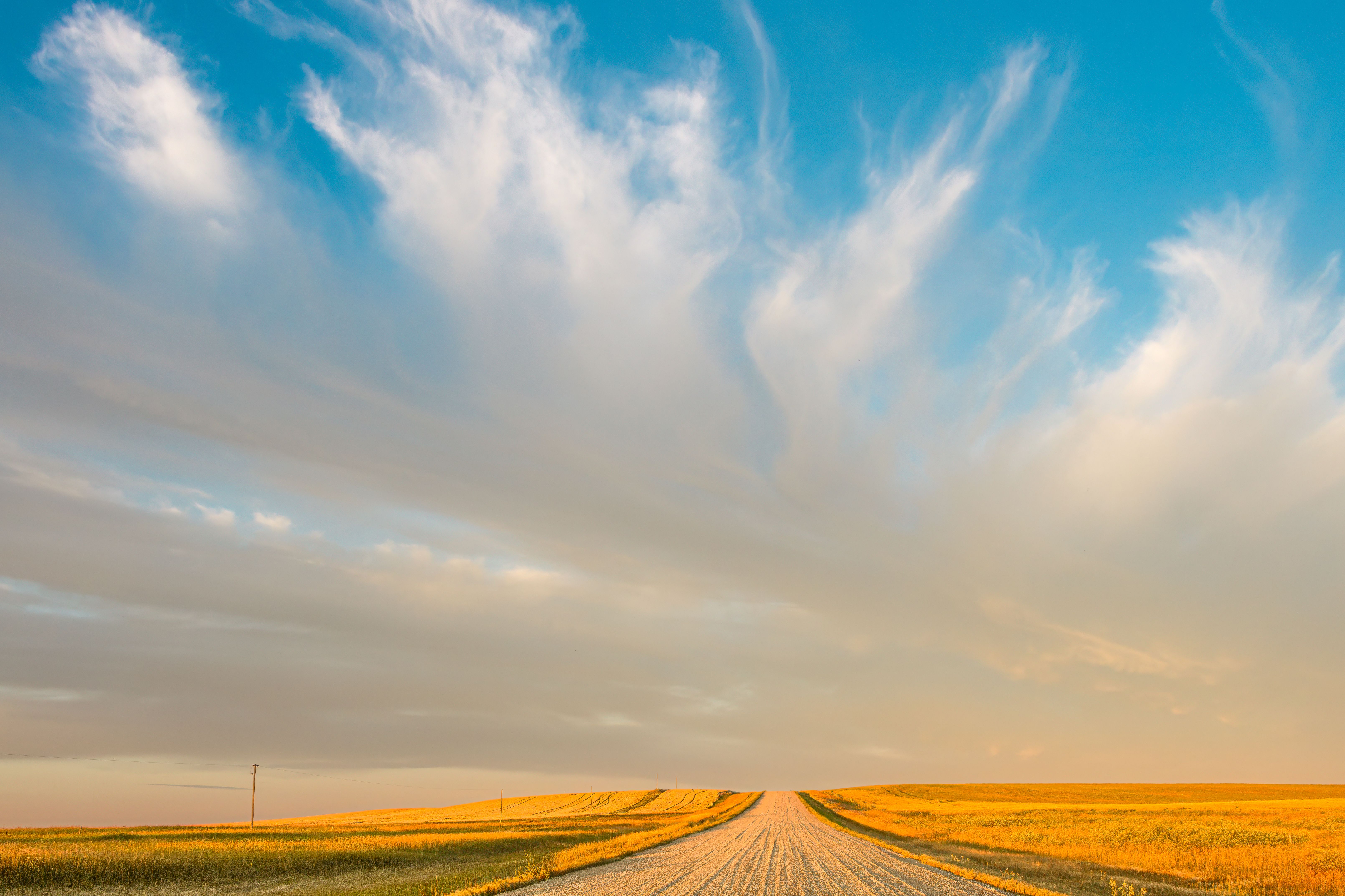 A vast prairie landscape with a rural road and dramatic clouds at sunset