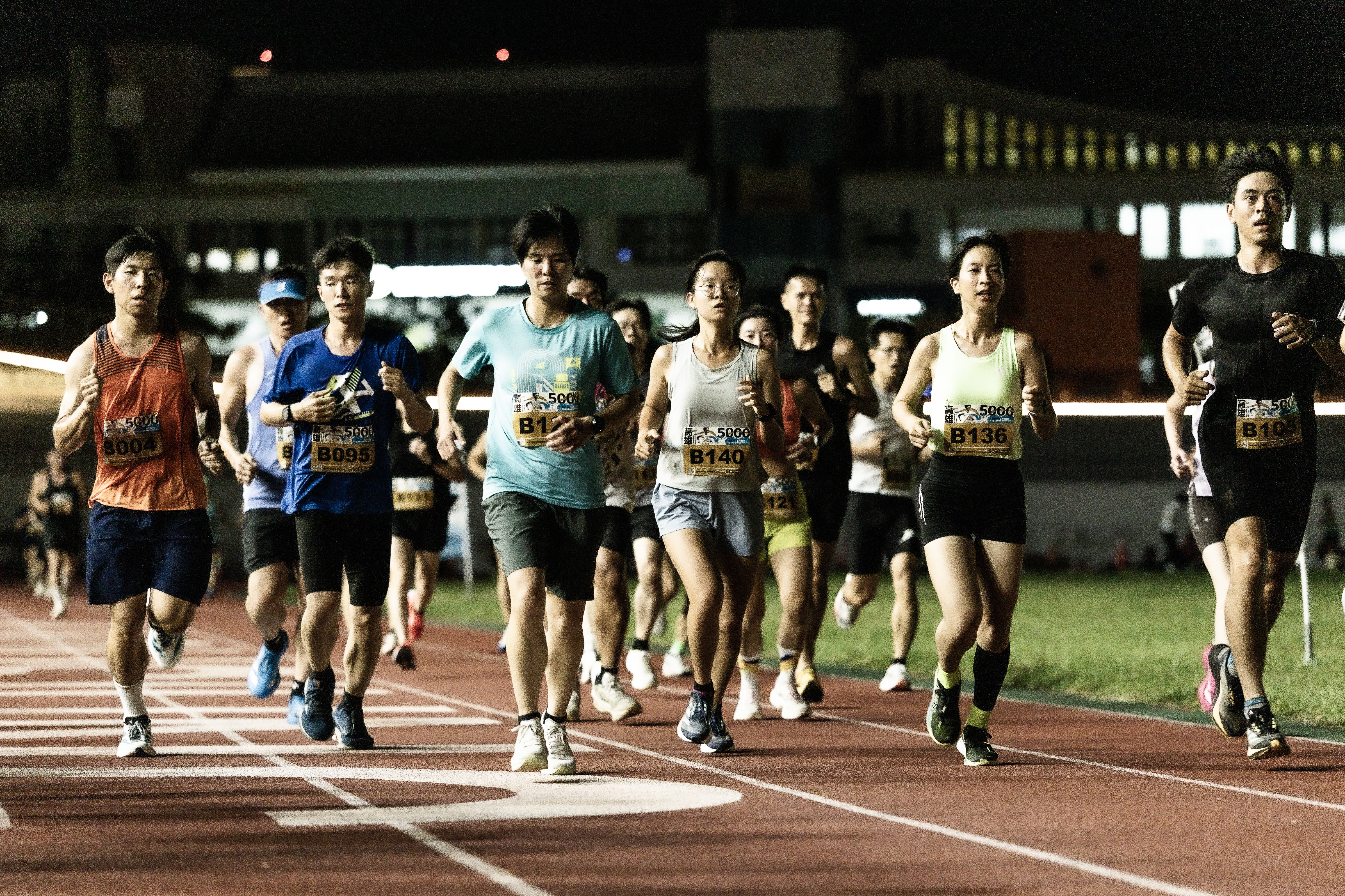 A diverse group of runners participating in a nighttime marathon on an illuminated track.