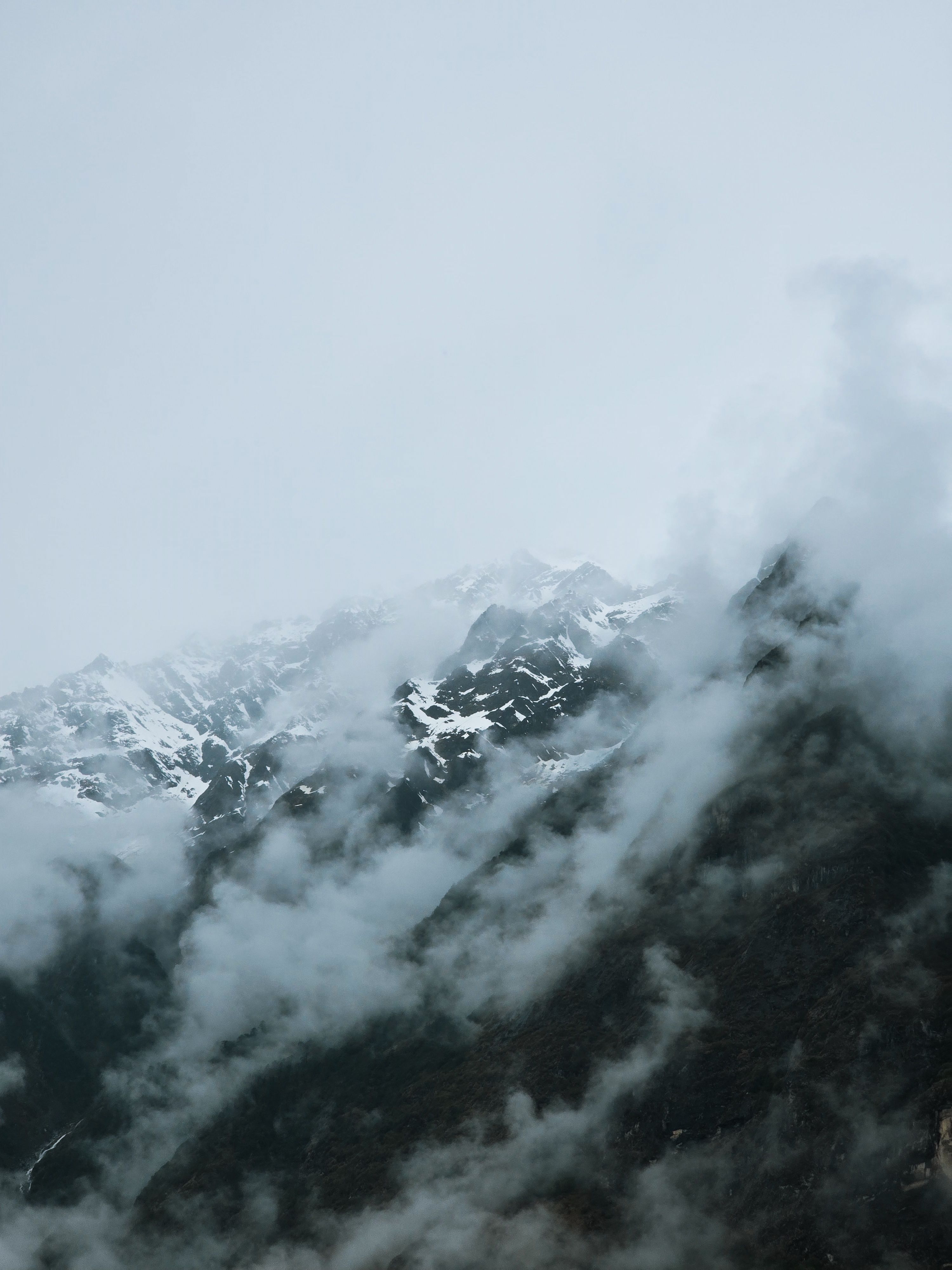 Captivating view of mist-covered snow-capped mountains under a cloudy sky.