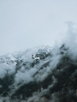 Captivating view of mist-covered snow-capped mountains under a cloudy sky.