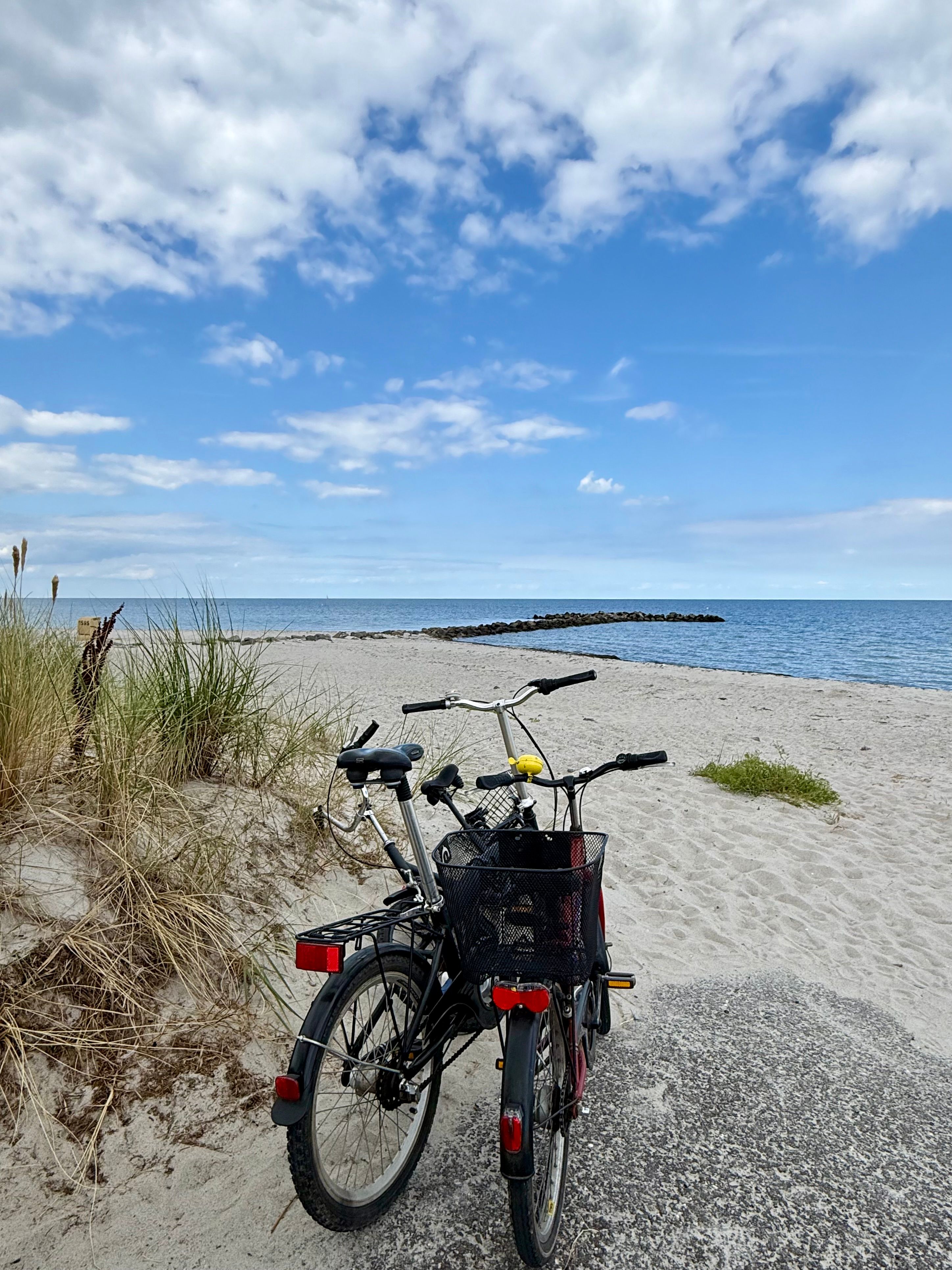Two bicycles parked on a sandy beach by the Baltic Sea under a partly cloudy sky, ideal for summer scenes.