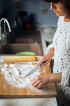 Woman skillfully prepares traditional homemade dumplings on a wooden chopping board in a kitchen.