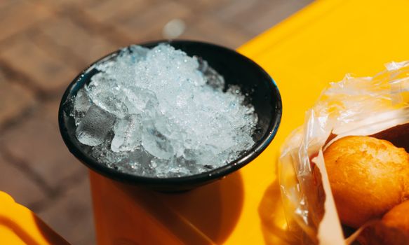 Black bowl filled with ice beside fried pastries on a yellow table.