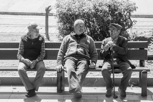 Free Black and white photo of three senior men conversing outdoors on a sunny day. Stock Photo