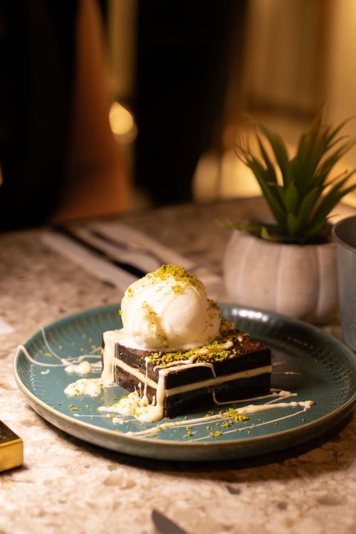 Free Delicious chocolate brownie topped with vanilla ice cream and crushed pistachios on a ceramic plate. Stock Photo