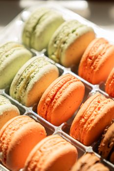 Vibrant macarons in pastel and warm tones arranged in a sunlit display, perfect for dessert themes.