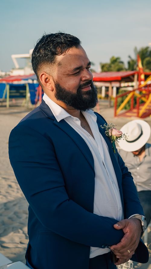 Free A man in a blue suit with a boutonniere smiles at a beach wedding celebration. Stock Photo