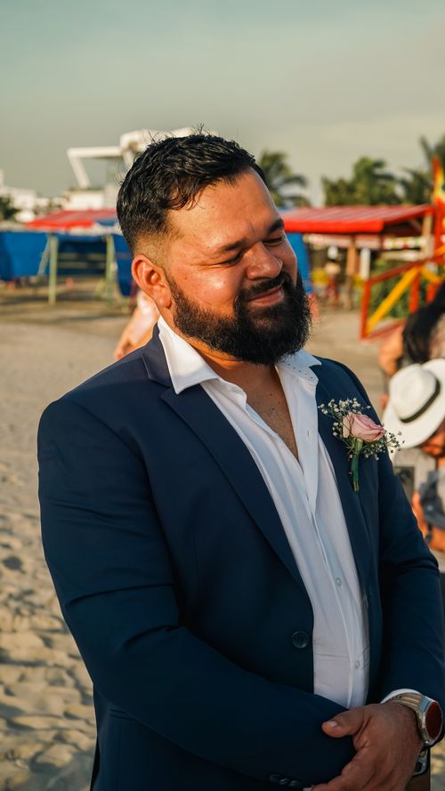 Free A smiling man in formal attire enjoying a sunny beach event, creating a joyful atmosphere. Stock Photo
