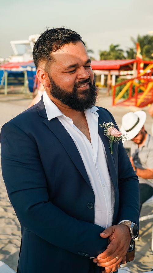 Free A man in a navy suit smiles during a sunny beach ceremony with colorful background. Stock Photo