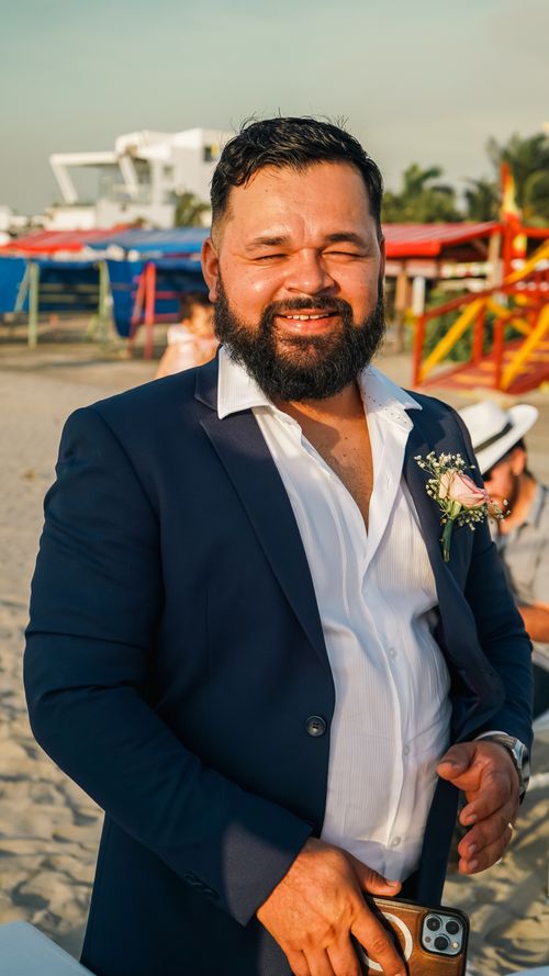 Free A cheerful man in a suit with a boutonniere, enjoying a sunny day at the beach. Stock Photo