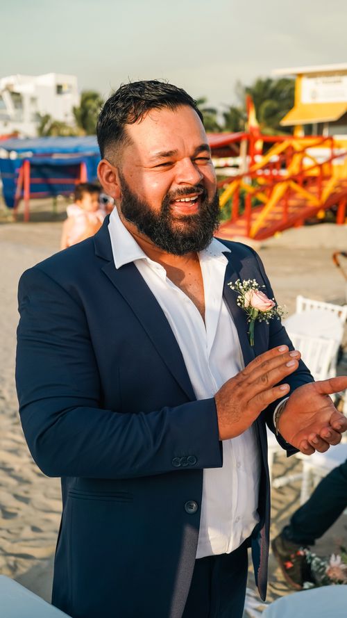 Free Smiling man in a suit enjoying a sunny beach wedding celebration with vibrant decorations. Stock Photo
