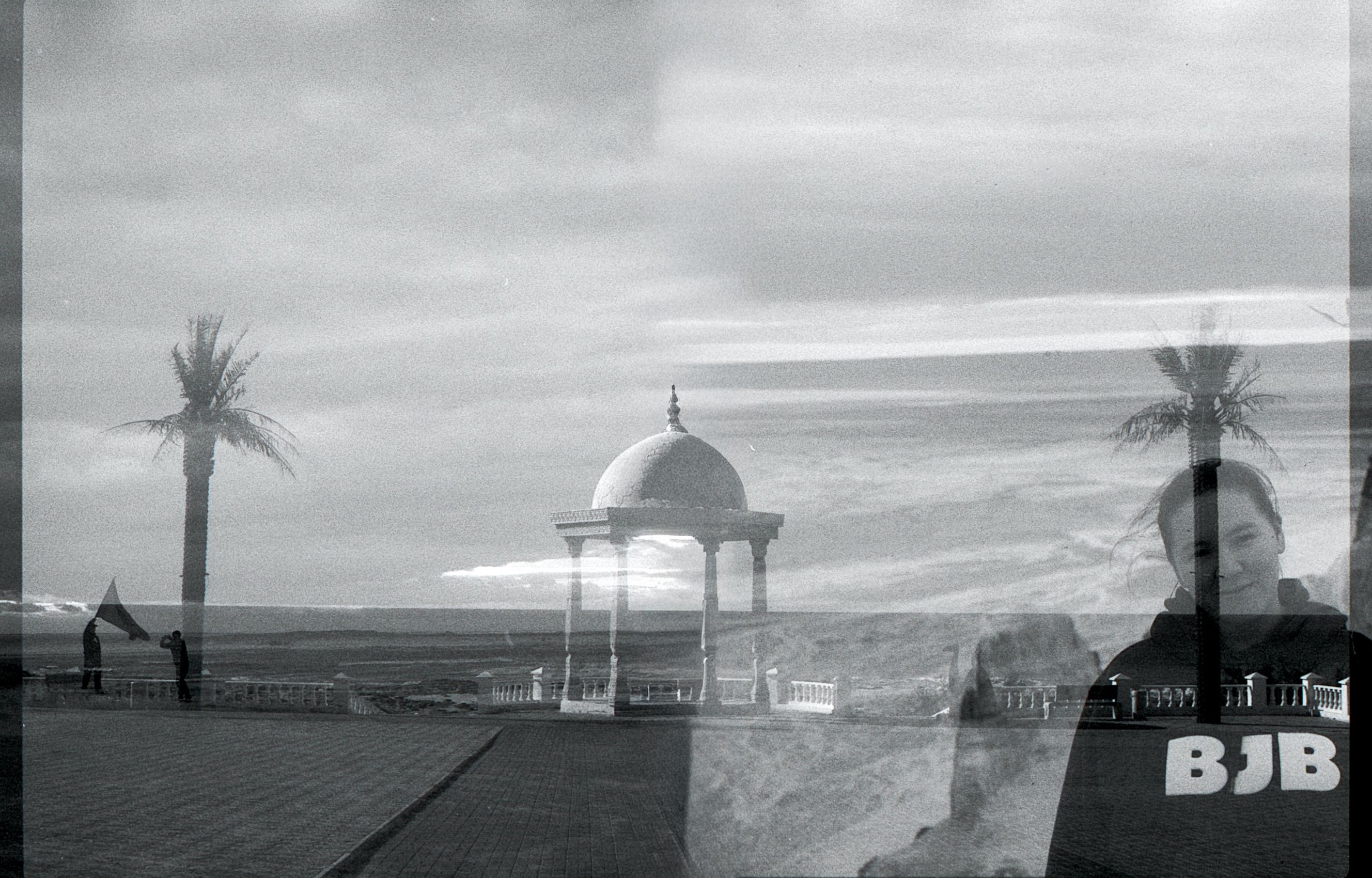 A creative black and white double exposure of a landscape with pavilion and palm trees mixed with a person's portrait.