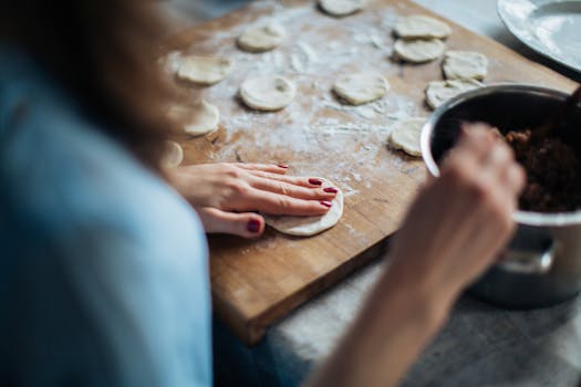 A person prepares homemade pastries on a wooden board with fresh dough and ingredients.