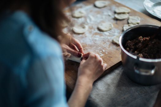 A woman skillfully prepares homemade dumplings on a wooden board, showcasing traditional culinary skills.