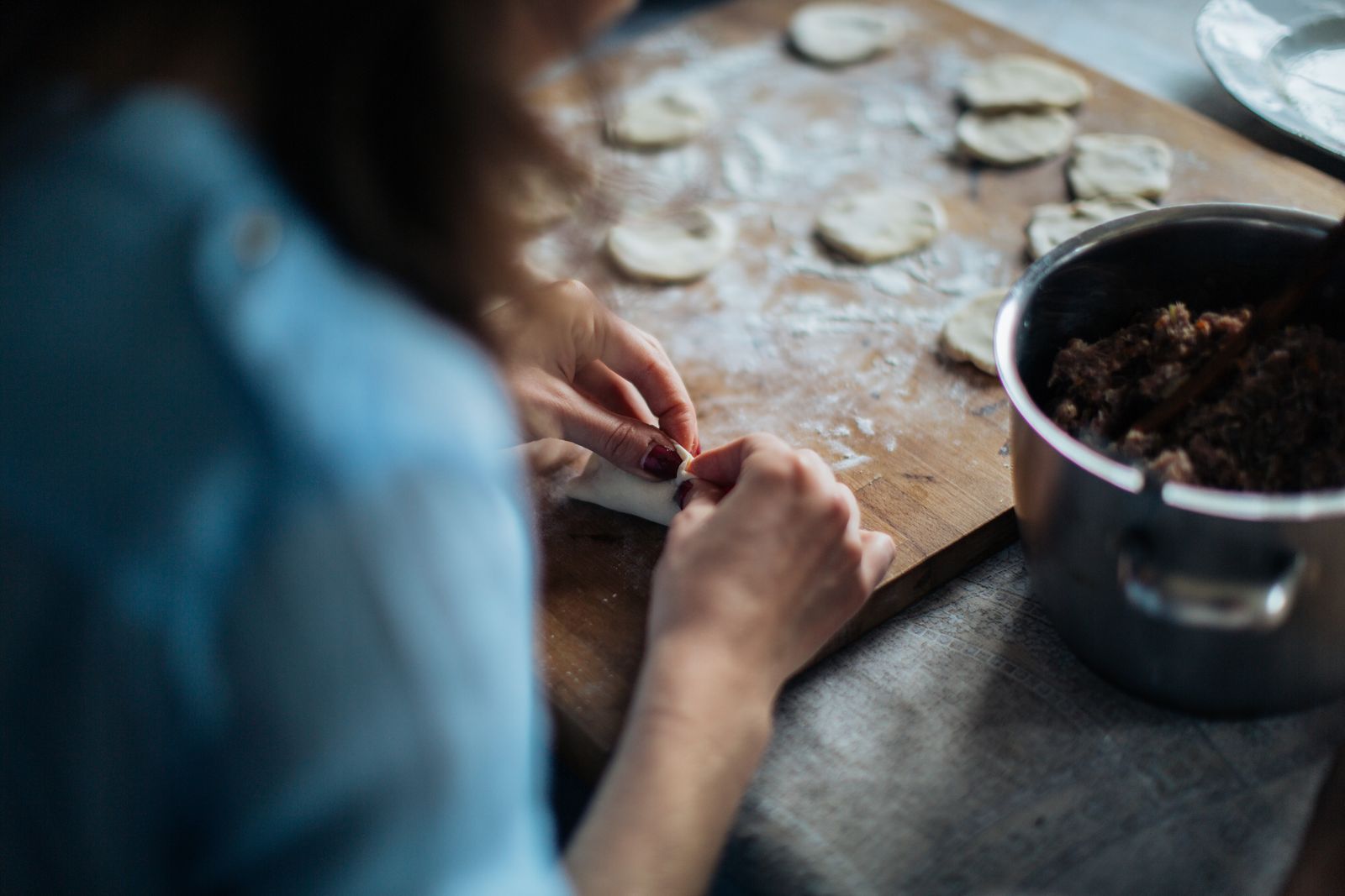 A woman skillfully prepares homemade dumplings on a wooden board, showcasing traditional culinary skills.