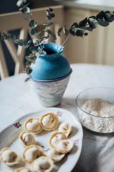 A cozy table setting featuring handmade pelmeni dumplings and a blue vase.