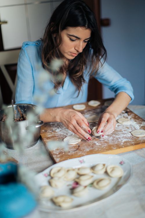Free A woman carefully prepares homemade pastries on a wooden board in a cozy kitchen setting. Stock Photo