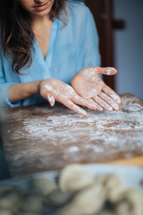Free Close-up of flour-dusted hands preparing traditional homemade pelmeni on a wooden table. Stock Photo