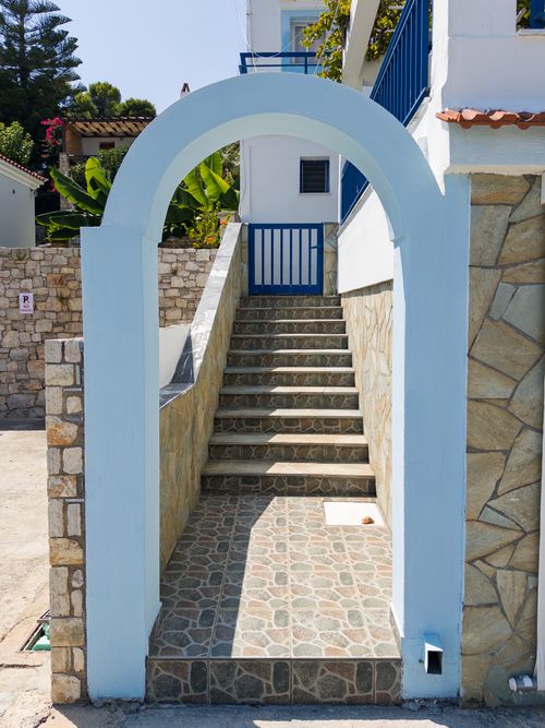 Free A picturesque stone archway leading to a Greek home, bathed in summer sunlight. Stock Photo