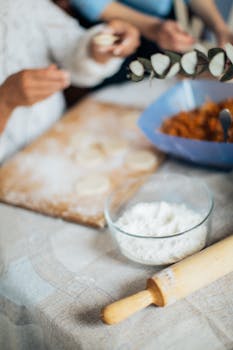 Hands preparing homemade dumplings with fresh dough, flour, and a rolling pin on the table.