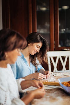 Two women preparing traditional pelmeni together in a cozy kitchen setting.