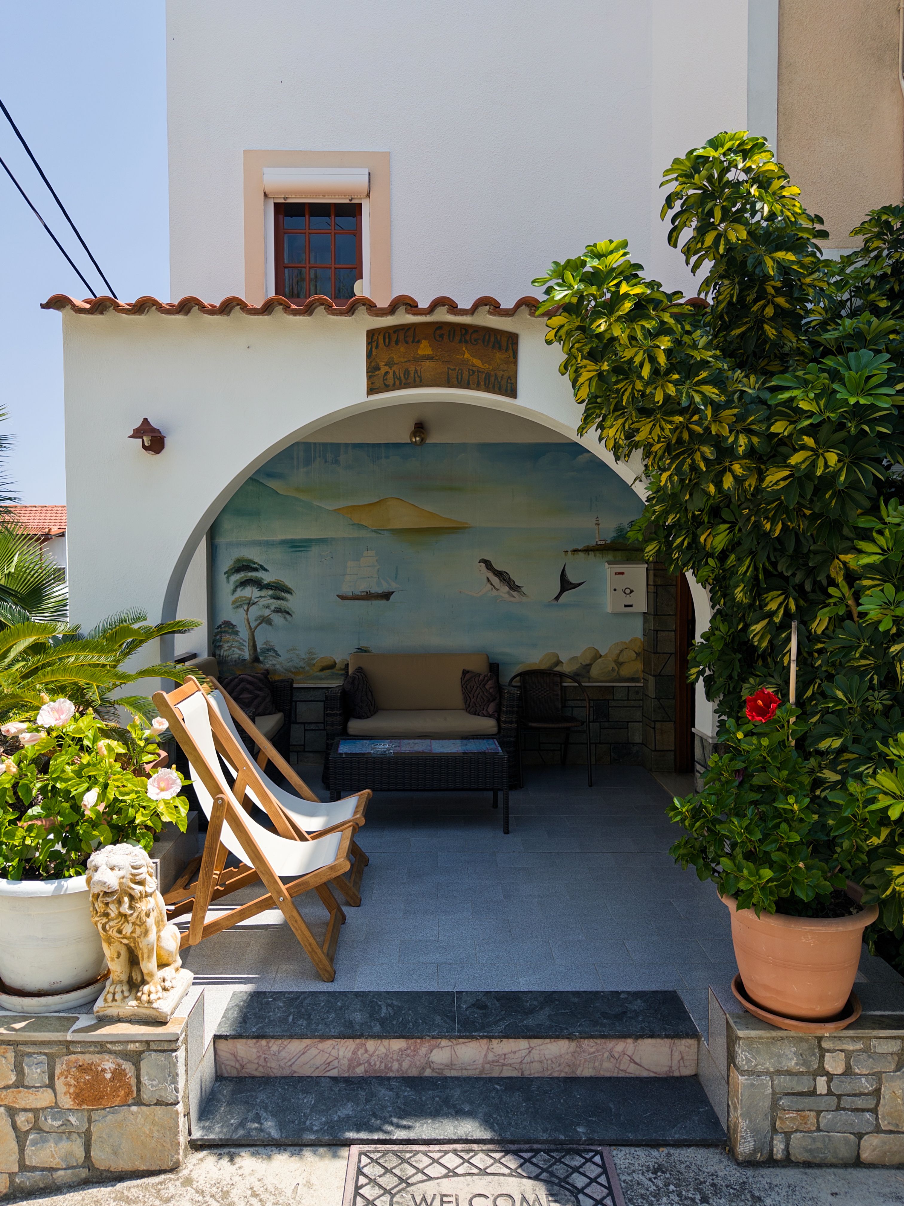 Cozy patio setting in Greece featuring a colorful mural, lush greenery, and comfortable seating.