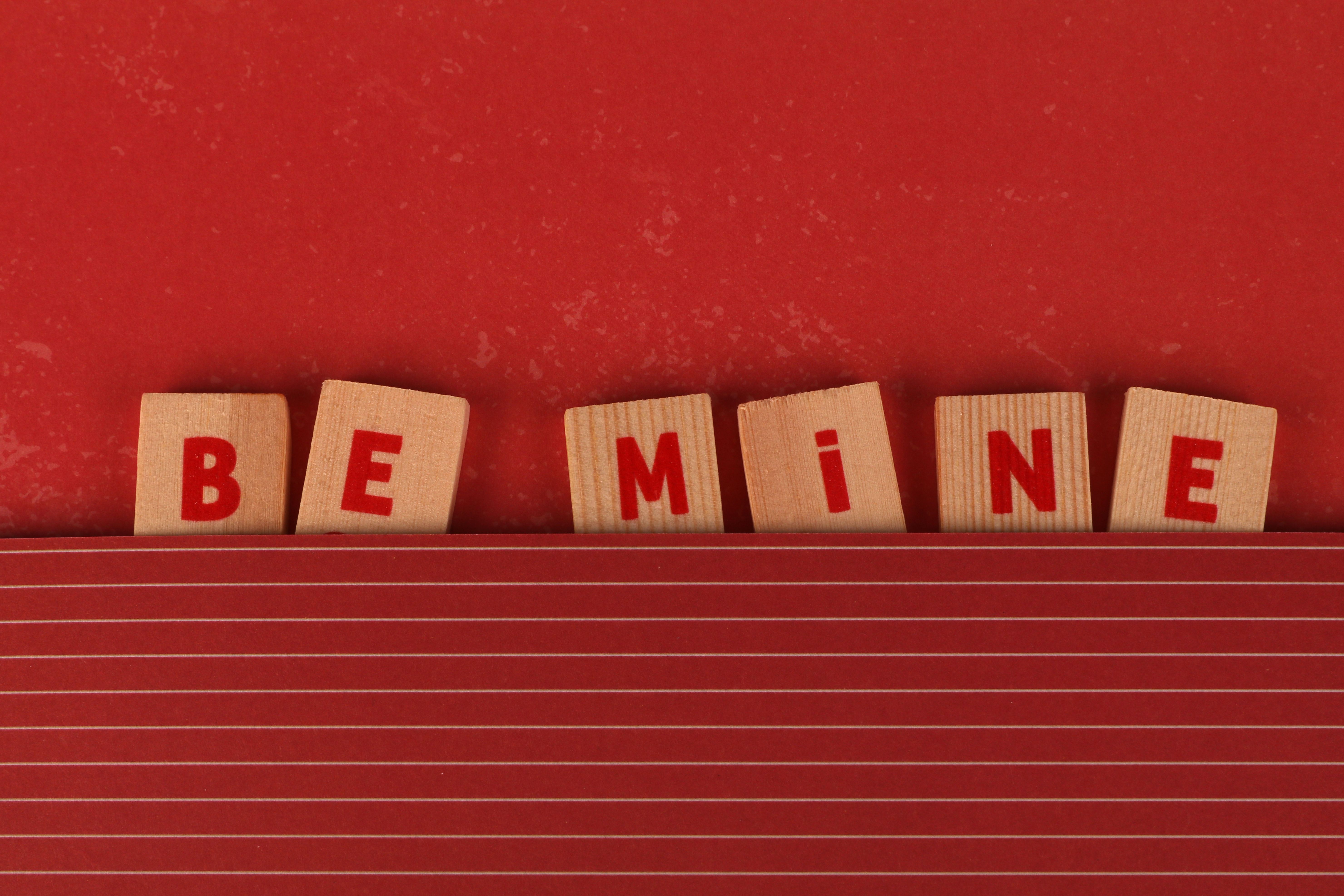 Red-themed Valentine's Day image with 'Be Mine' wooden tiles, perfect for romantic occasions.