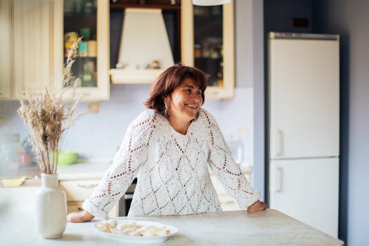 Smiling woman in white sweater enjoying a peaceful moment in her stylish kitchen.