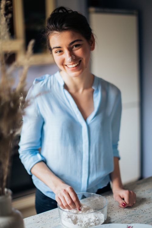 Free A cheerful woman in a blue shirt baking with flour in a cozy indoor setting. Stock Photo