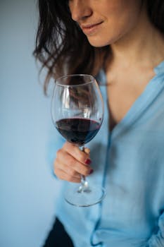 Woman holding a glass of red wine, enjoying a relaxed moment indoors.