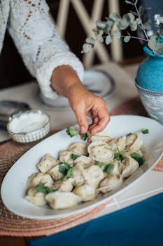 Hand placing herbs on a dish of homemade dumplings, adding a fresh touch.
