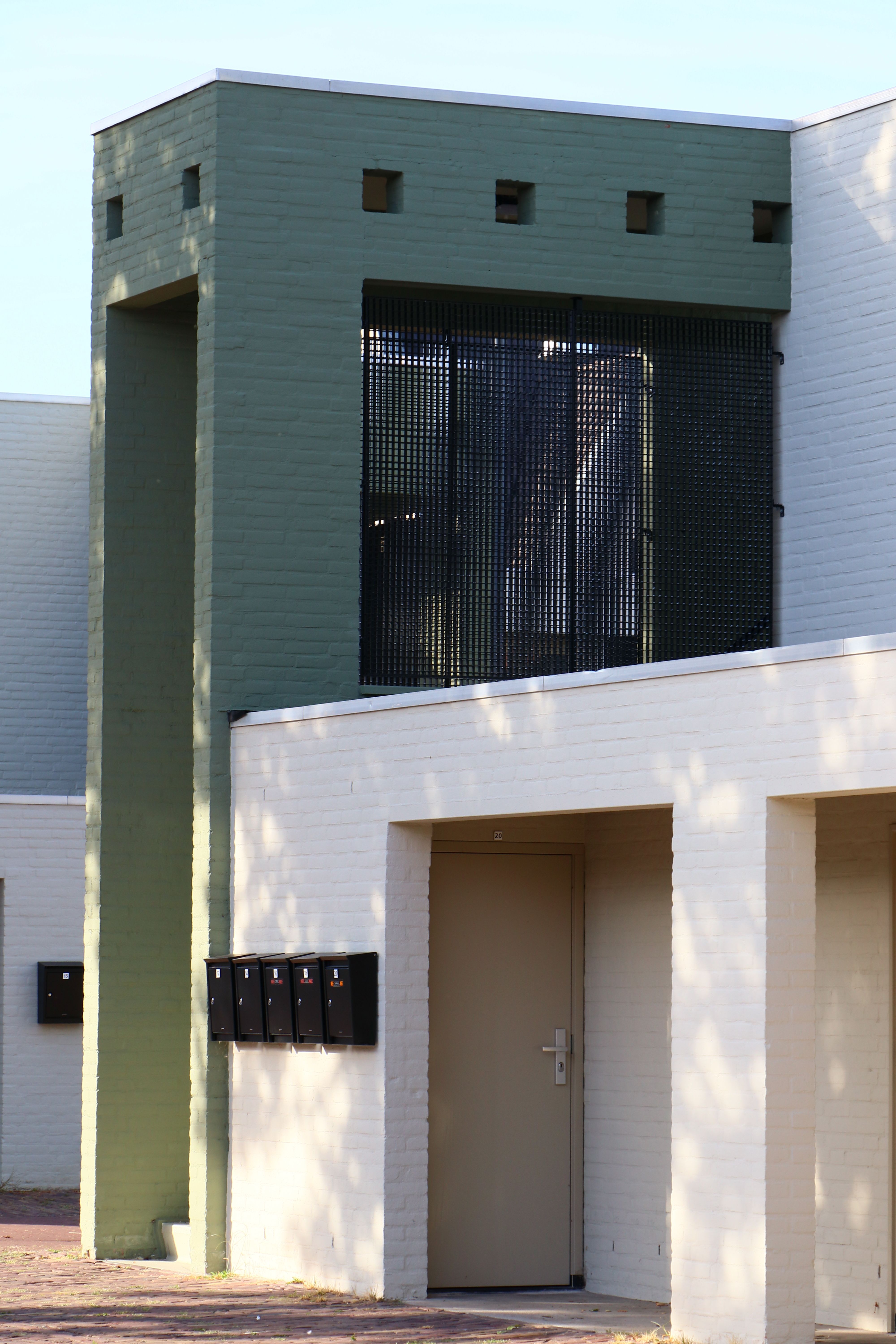 Modern building with green facade and multiple mailboxes, captured in bright daylight.