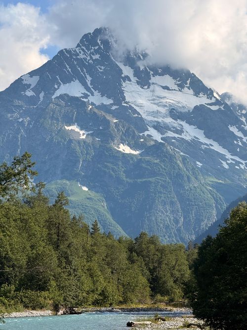 Free Stunning view of a snow-capped mountain in summer with a clear blue river and green forest foreground. Stock Photo