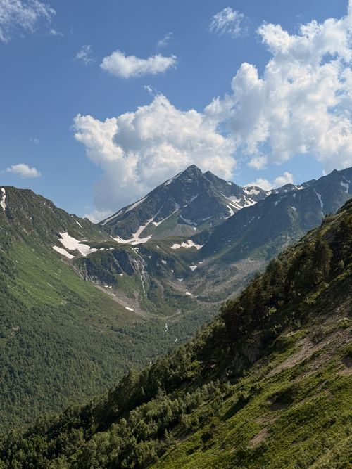 Free Breathtaking view of snow-capped Caucasus mountains and lush green valleys under a blue sky. Stock Photo