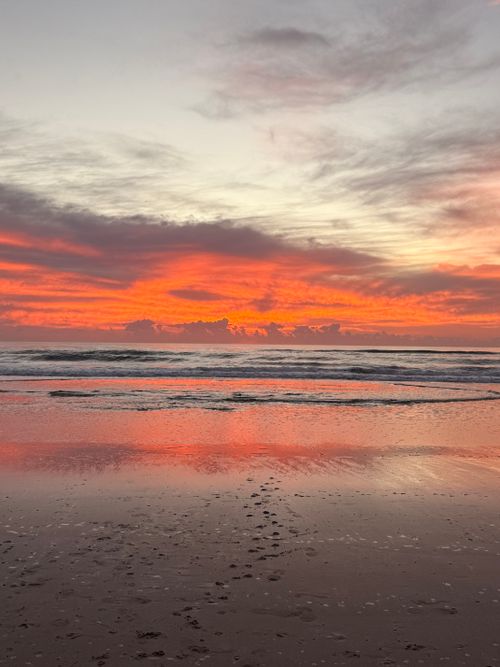 Free Vibrant orange sunrise over the ocean with clouds reflecting on the water. Stock Photo