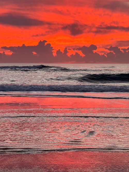 Free Stunning red and orange sunset reflecting on ocean waves, capturing nature's vivid colors at dusk. Stock Photo