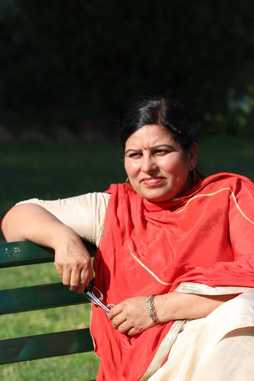 Free A woman in red and cream traditional attire seated on a park bench under sunlight. Stock Photo