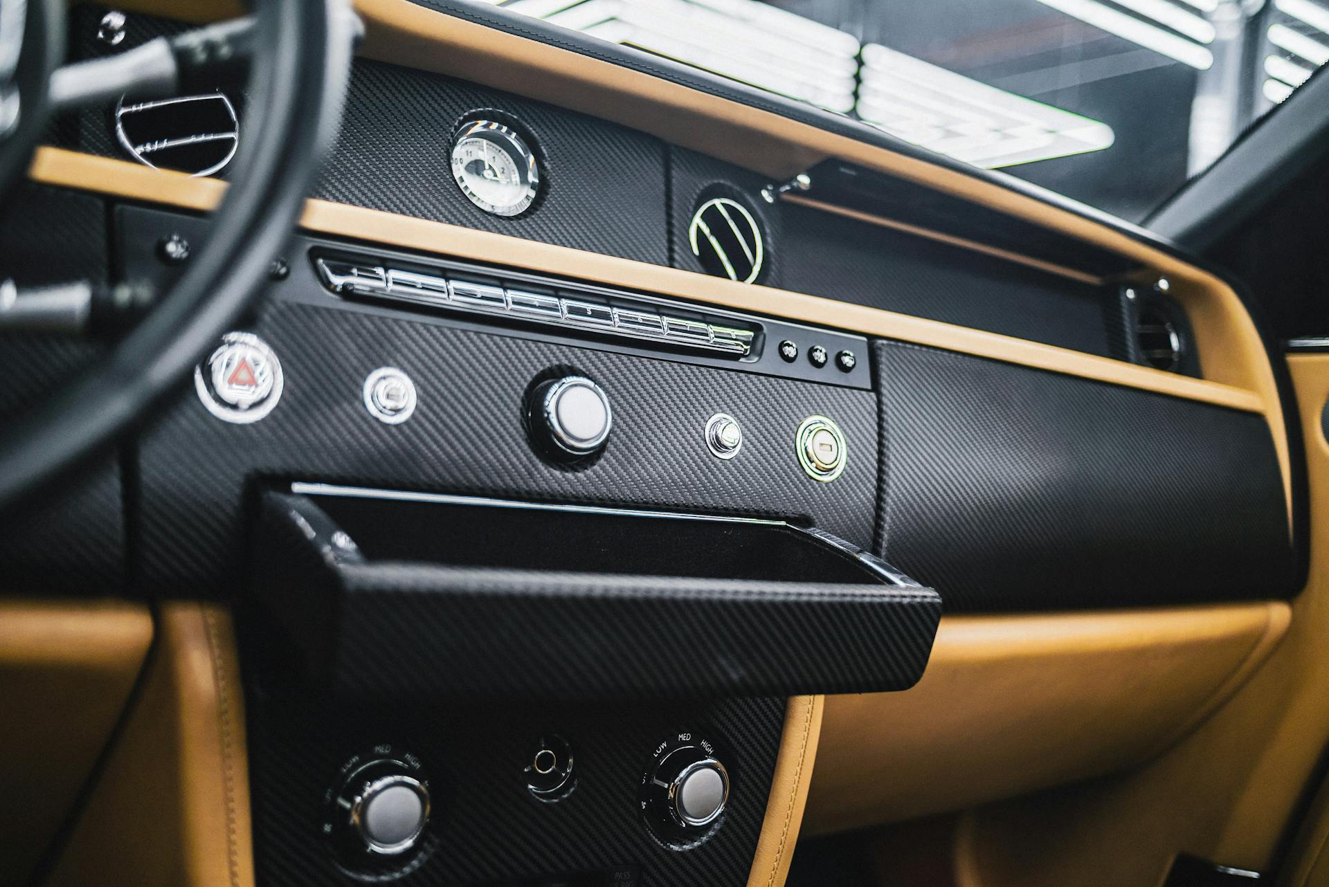 Close-up of a vintage car dashboard featuring carbon fiber trim and modern design elements.