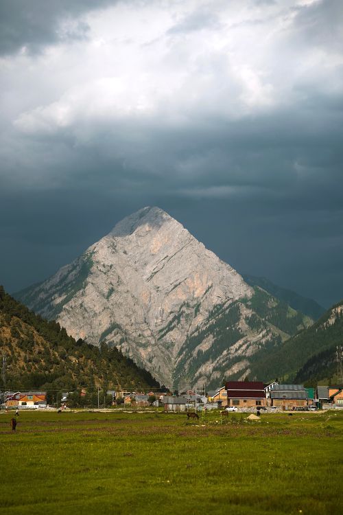 Free A towering mountain rises above a small, picturesque town under dramatic skies. Stock Photo