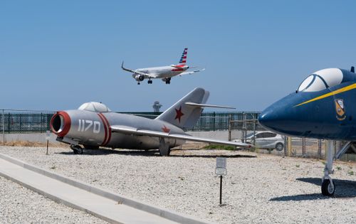 Free A vintage fighter jet museum with a modern commercial plane flying overhead in a clear blue sky. Stock Photo