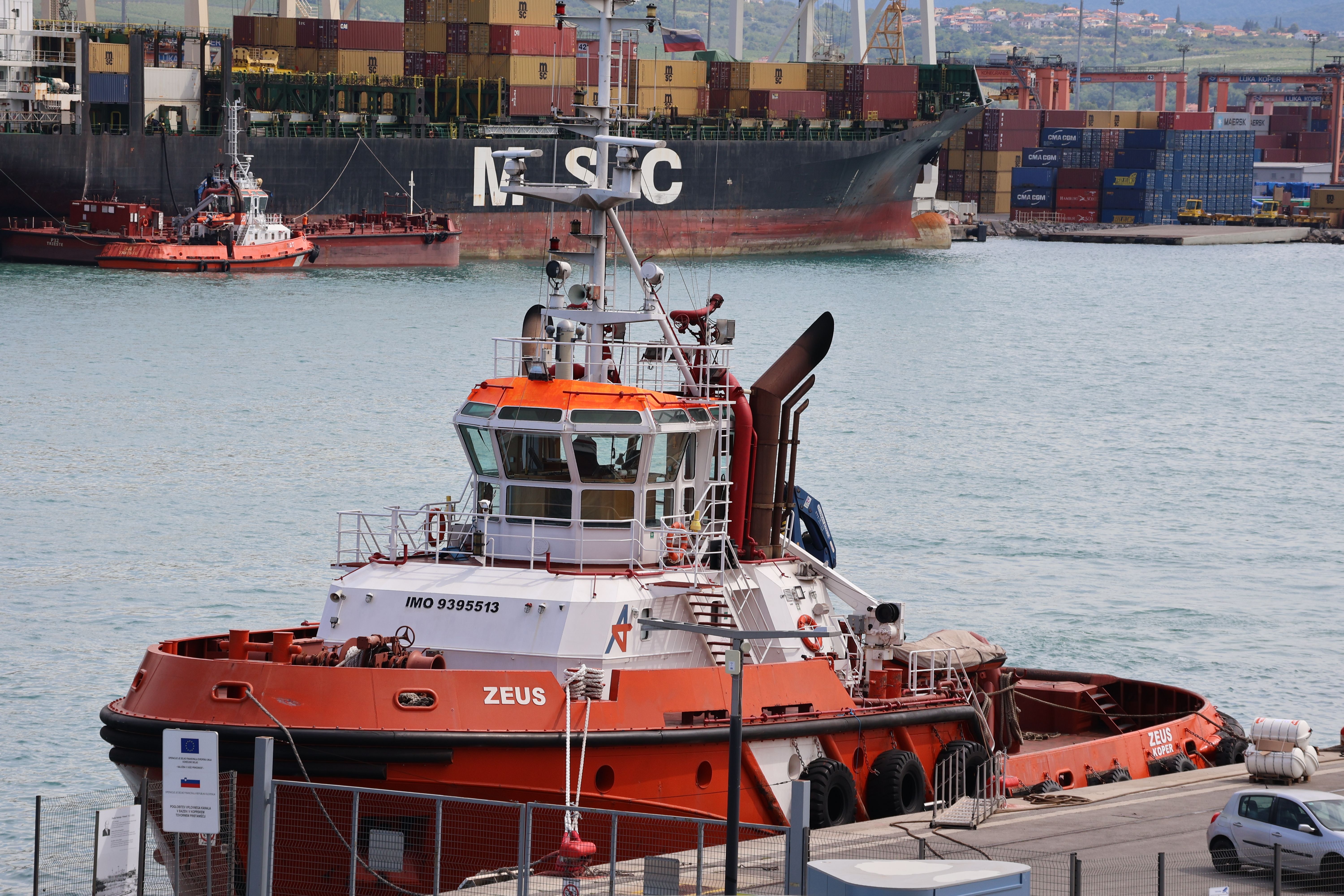 Illustrative photograph: Tugboat Zeus docked at Koper Harbor, Slovenia, with a view of the cargo ship at the port.