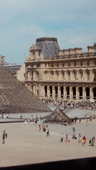 A bustling scene of the Louvre Museum and pyramid in Paris on a sunny day.
