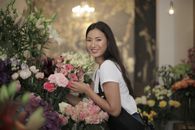 花店里，一位面带微笑的店员正摆放着各式各样的鲜花